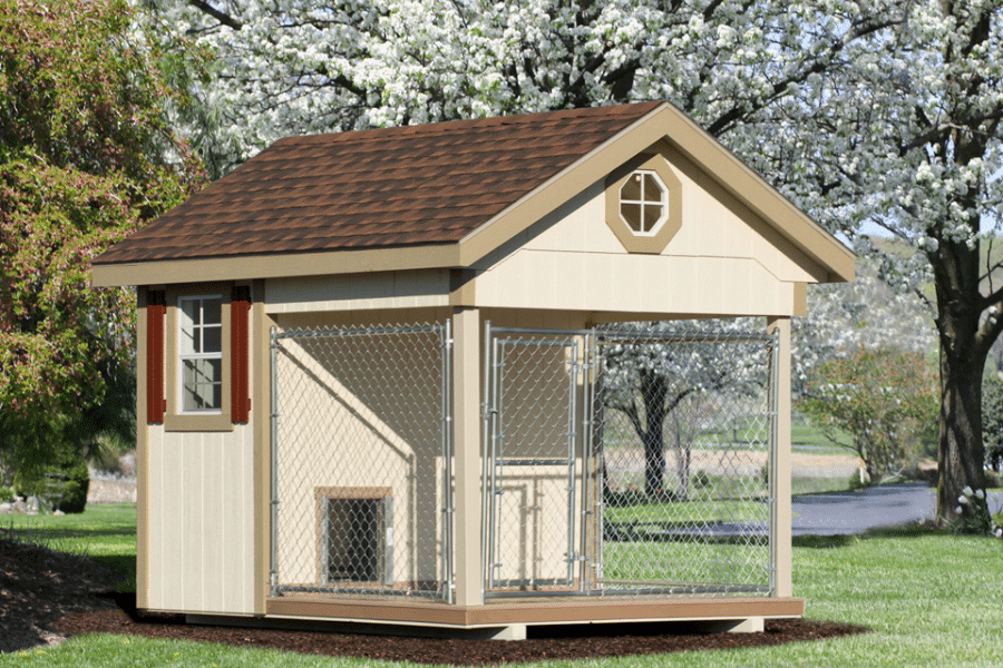 light and dark tan trimmed kennel with reddish brown shingle roof and an attached chain link run
